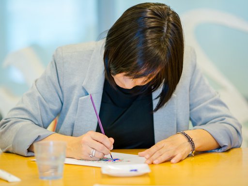 A photograph of a lady with her head down working on a painting