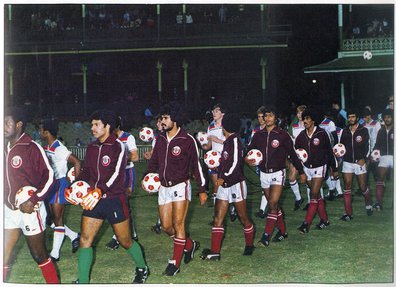 Football team wearing maroon zip up jumpers walk onto a pitch.