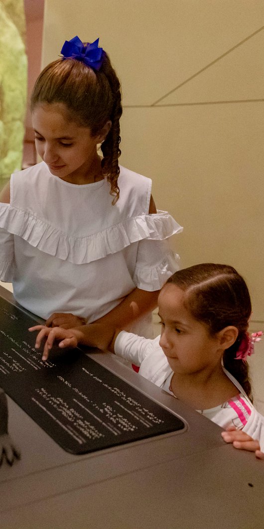 Two children use tactile accessible information panels at NMoQ