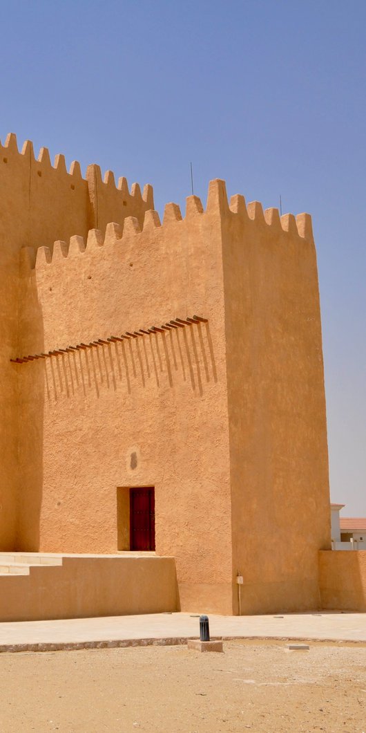 A tall angular tower made from sand coloured material with an open doorway and crenellations around the top of the building