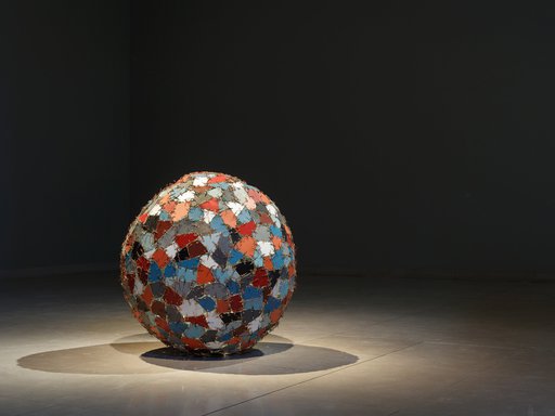 A spotlight on the object Chaos+Repair=Universe showcasing a sculpture with coloured mirror fragments stitched into a ball shape with metal wires