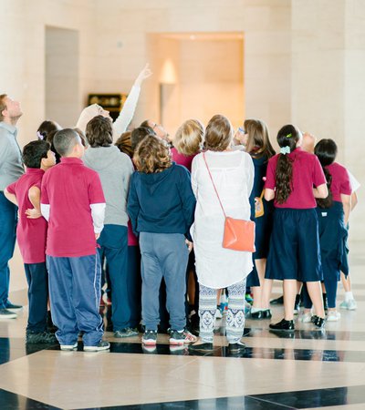 A photograph of a group of children standing in the lobby of MIA looking skywards