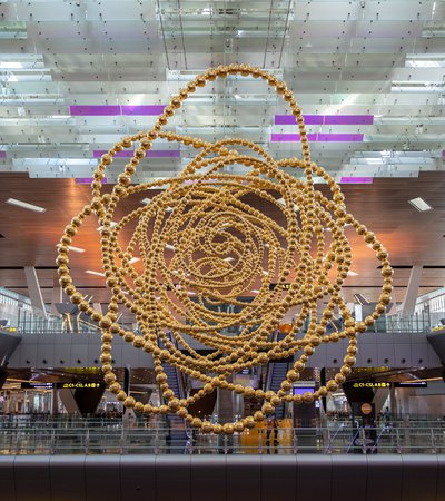 A large golden sculpture 'Cosmos' constructed of many concentric circular shapes suspended from the ceiling within an airport terminal