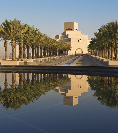 The main approach to the Museum of Islamic Art with palm trees on either side and its facade reflected in water