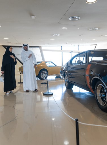 A man in Thobe and a woman in Abaya looking at the American muscle cars exhibited at NMoQ
