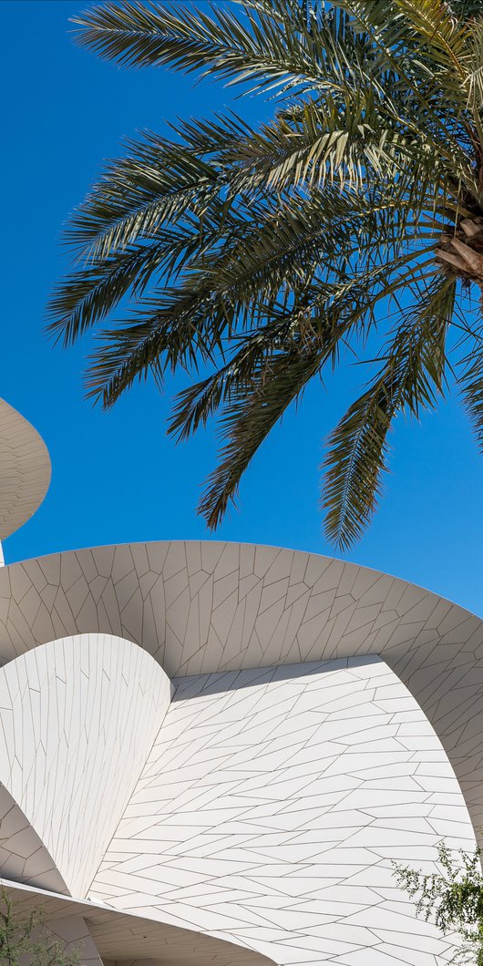 Decorated stone arches with a doorway in shade and a view of the National Museum of Qatar in the background