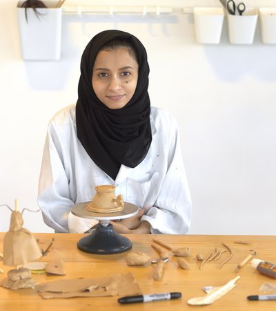 Hana Al Saadi sitting in a workshop surrounded by fresh clay objects