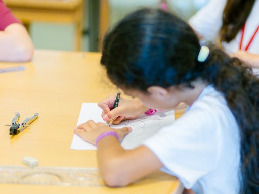 A girl sketches out geometric shapes on a white piece of paper for her kufic calligraphy