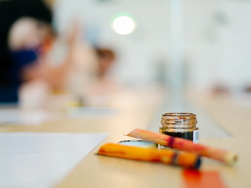 A close-up shot of a dip pen and coloured ink with workshop participants blurred in the background