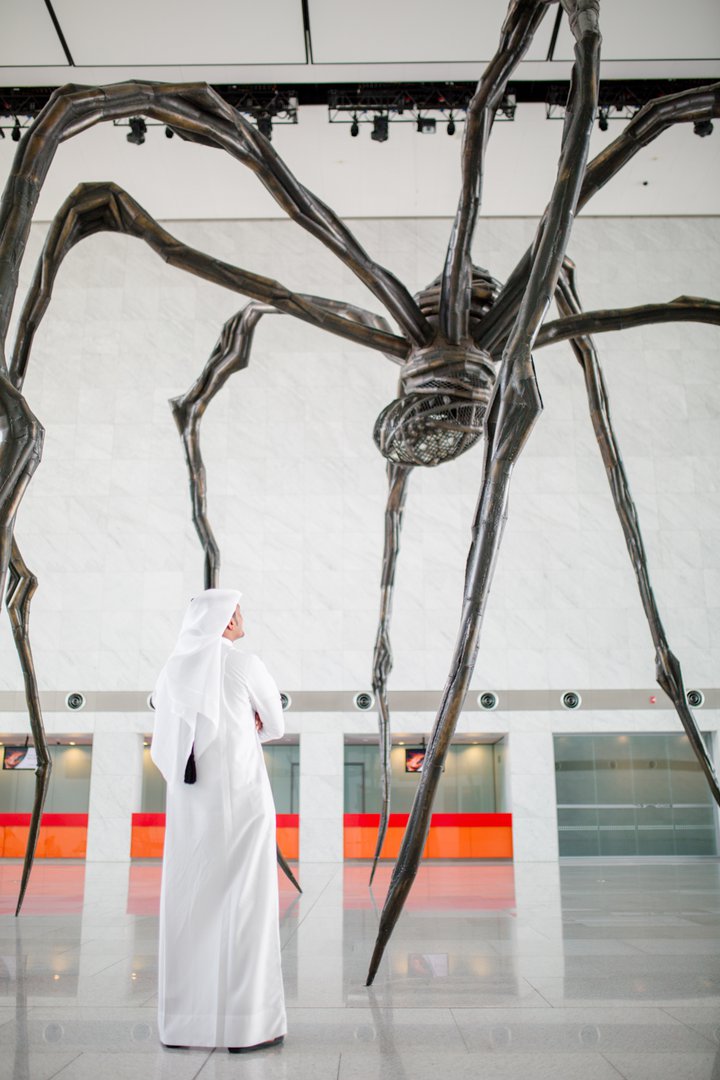صورة لزائر يقف بجوار منحوتة ماما الضخمة في مركز قطر الوطني للمؤتمرات