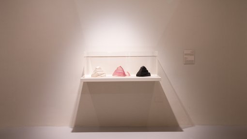 Gallery view of three pyramids, white, pink and black, in a see-through case.