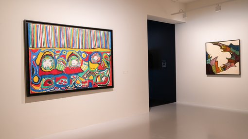 Two colourful paintings hang against a corner of white walls in a gallery space.
