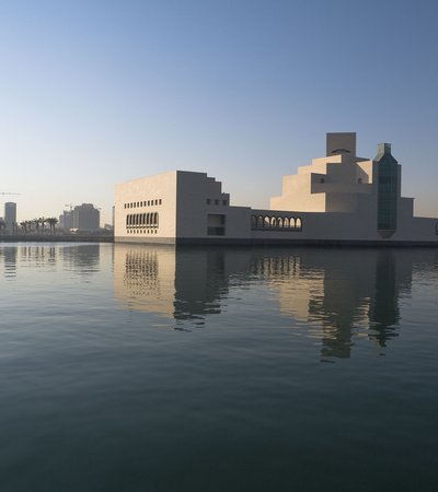An exterior view of the Museum of Islamic Art during the day, showing the building's reflection in the water