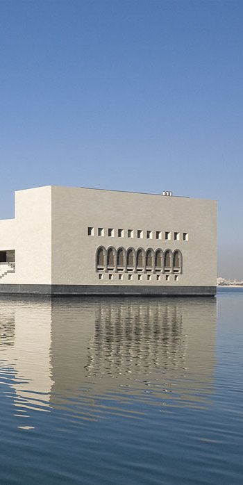View of the Museum of Islamic Art from the quayside with water and an avenue of palm trees