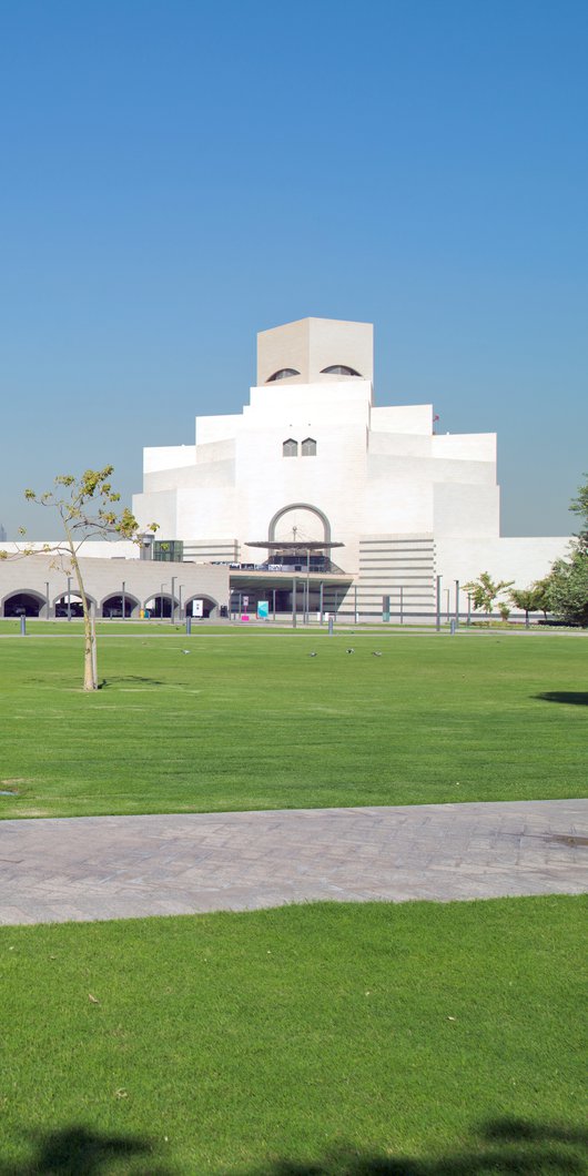 An open parkland space with green grass and native trees and the Museum of Islamic Art in the background