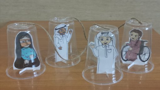 Drawing cutouts representing four characters in traditional Qatari costumes under plastic cups
