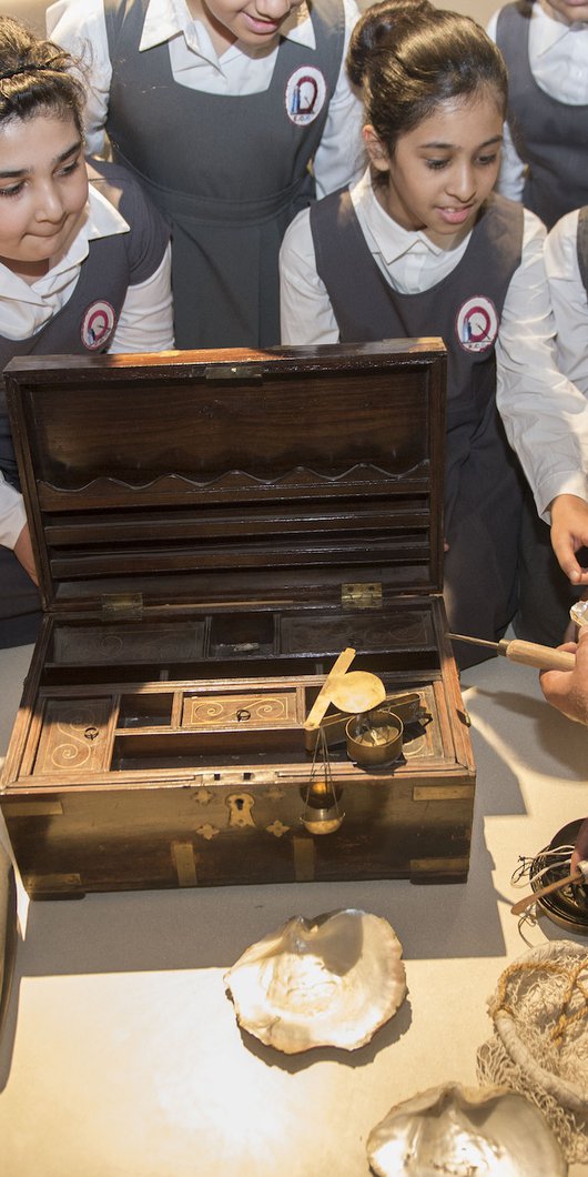 Students observing a man handling an old pearl diving kit