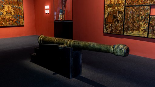 Picture of the gallery of 'One Tiger or Another' exhibition, showing a cannon, a weapon and a collection of paintings