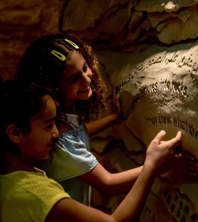 Two smiling children exploring the wall carvings in NMoQ's Cave of Wonders