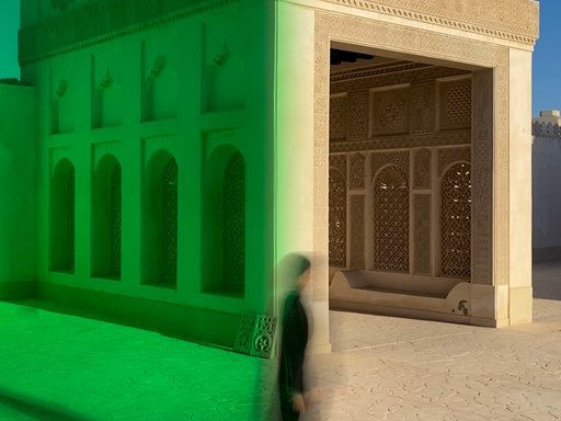 A contemporary image of a woman in black walking in front of a Qatari historic building.