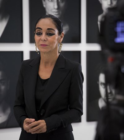 Portrait of the artist Shirin Neshat standing in Mathaf: Arab Museum of Modern Art, while being interviewed alongside a backdrop of her art
