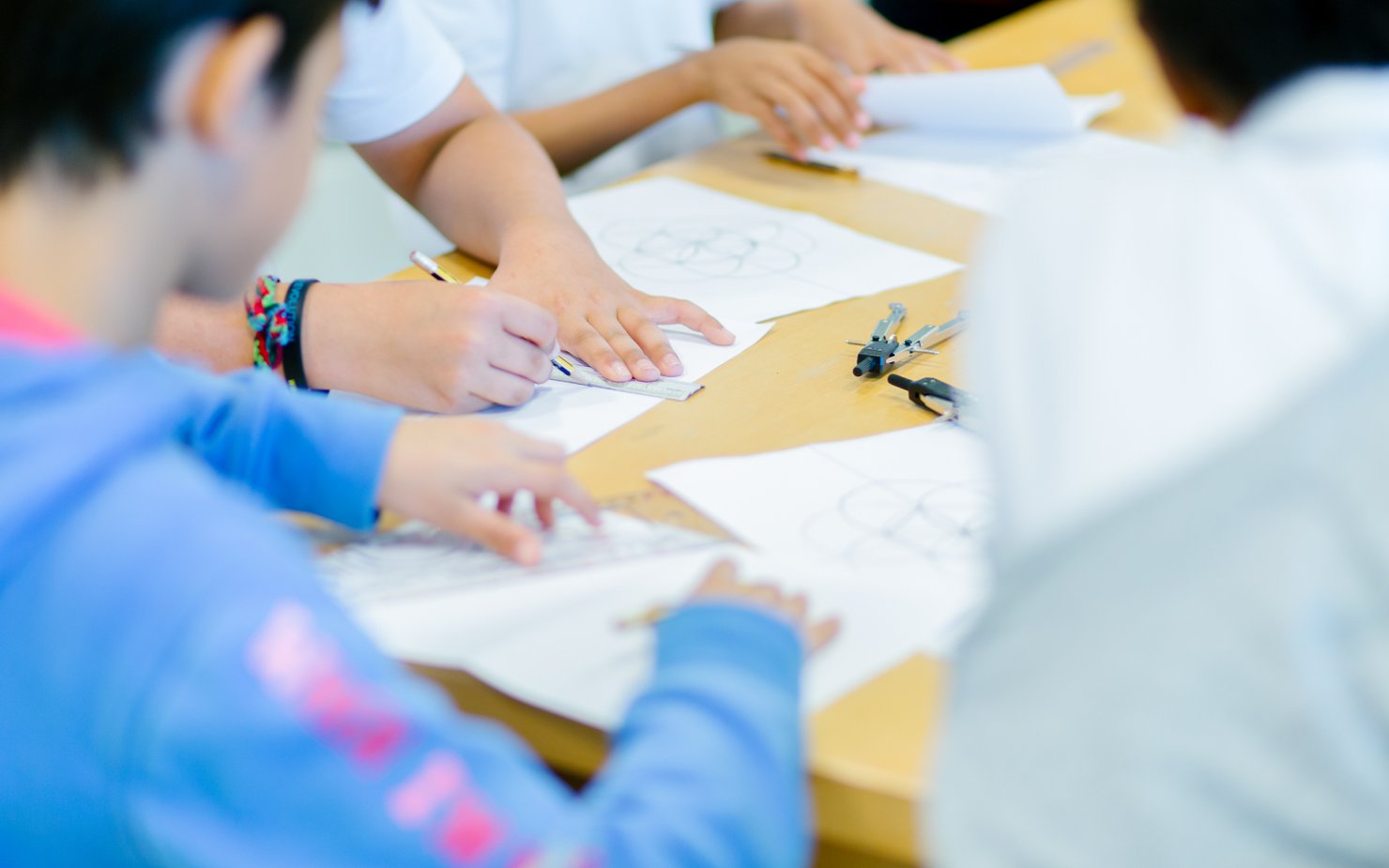 A group of children circled around a table, sketching out geometric shapes