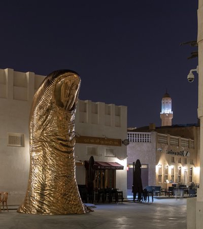 A bronze thumb sculpture in the middle of Souq Waqif, with a number of buildings and cafes in the background.